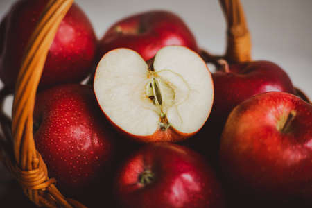 Ripe large red fruits of sweet apples lie in a wicker wooden basket. One apple is cut in half. Diet and vegetarianism. Fruit harvesting. Healthy nutrition.の写真素材
