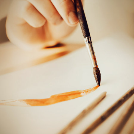 The artist holds a paintbrush in his hand and draws a line on paper with orange paint on a sunny day. The creative process. inspiration.の写真素材