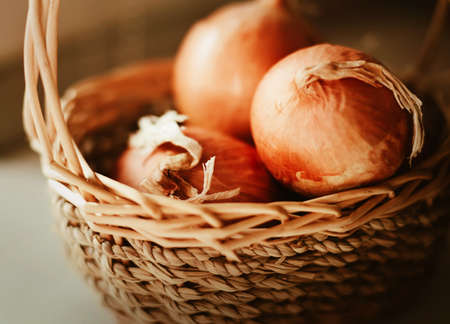 In a small wicker basket there are three ripe onion bulbs on a sunny day. Harvesting and agriculture. Healthy food and vegetables.の写真素材