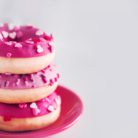 On a small red saucer are three pink delicious sweet donuts with colorful sprinkles. beautiful dessert. bakery products. junk food.の写真素材