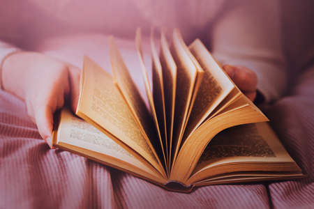 A man is lying on a bed with a pink soft blanket and flipping through the pages of an old interesting book. reading literature. self-development.の写真素材