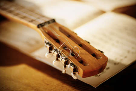The fretboard of an old vintage acoustic guitar with metal strings lying on a wooden table next to sheets of sheet music. Solfeggio and music lessons on a sunny day. A musical instrument.の写真素材