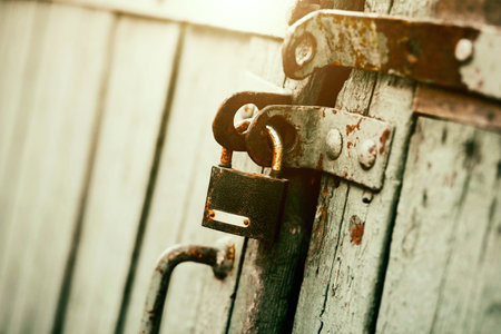 An old rusty padlock closes the wooden old gate on a sunny day. closed. safety.の写真素材