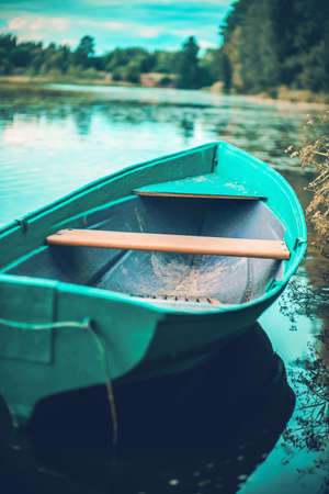 A blue empty fishing boat floats on the surface of the water in the river near the shore against the background of the forest and the blue sky on a summer day. Recreation and fishing.の写真素材