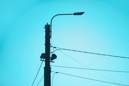 A dark silhouette of a street lamp against a clear blue sky. Street lighting and electrification. technologies.の写真素材
