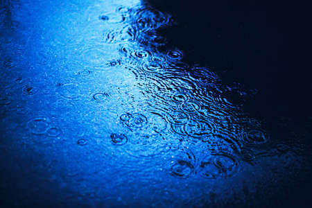 A deep puddle on the asphalt in the city, on the surface of which raindrops fall. bad weather. rainy evening.の写真素材