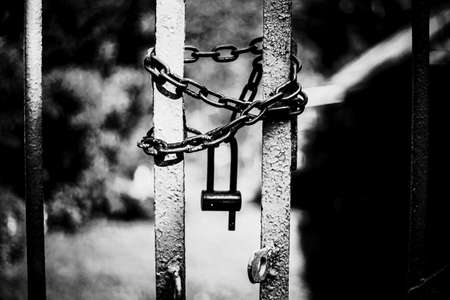 A black-and-white image of an old gate closed with a rusty chain and padlock. Private territory.