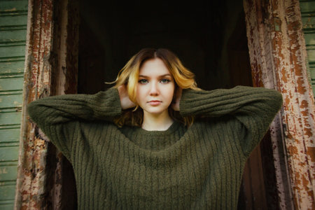 Portrait of a beautiful blonde woman in a vintage sweater posing in the doorway of an abandoned old...