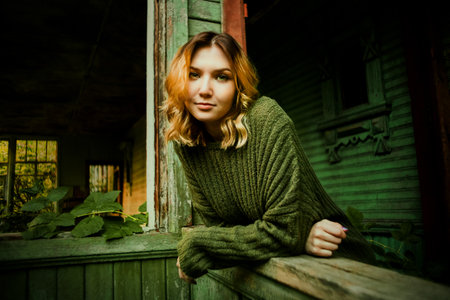 Portrait of a beautiful blonde woman in a green vintage sweater in an old wooden abandoned house...