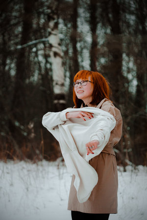 Portrait of a cheerful beautiful ginger Asian woman who wears a white hoodie while walking in a winter park. Warm clothes and cold weather.の写真素材