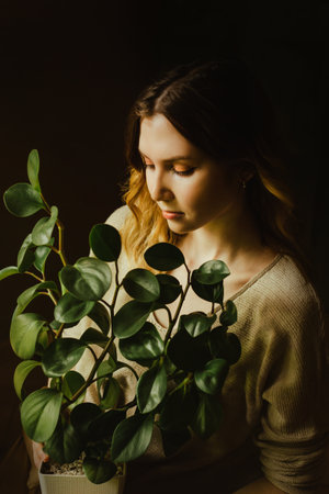 Portrait of a beautiful blonde who gently holds a potted plant with green leaves in her hands. Home gardening and love of plants. nature protection and ecology. indoor plants.の写真素材