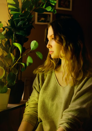 Portrait of a beautiful young blonde woman who is sitting at home in the evening near indoor green plants. Home gardening and love of plants. Ecology.の写真素材