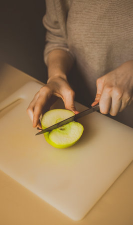 A woman cuts a ripe green apple on the kitchen board with a sharp knife. cutting fresh fruit. Health nutrition. Diet.の写真素材