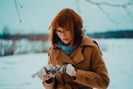 Portrait of a beautiful young red-haired Asian woman who takes off woolen gloves on a frosty winter day in the park. North.の写真素材