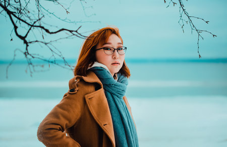 Portrait of a beautiful young red-haired Asian woman in winter clothes, who stands near the frozen sea in the park on a winter day. Travel in winter. North.の写真素材
