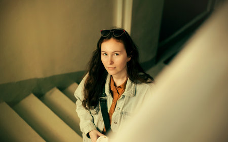 Portrait of a beautiful young female student who is climbing the stairs with a cup of coffee in her hands. Returning from a break. business lady.の写真素材