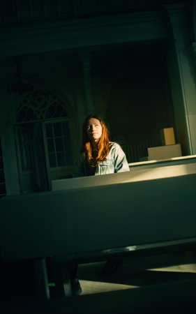Portrait of a beautiful young red-haired woman sitting on a bench in a dark Protestant church, illuminated by a ray of sunlight. religion and light.の写真素材