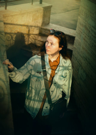 A view from above of a beautiful young woman in a denim jacket, who descends the stone steps of the building on a sunny summer day.の写真素材