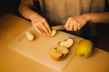 A woman on the kitchen board cuts ripe delicious apples with a knife. Health nutrition. A healthy diet. Fruit for breakfast.の写真素材