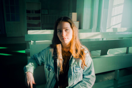 The red-haired young woman sitting in the church pews appears lost in thought. The scene suggests themes of faith, spirituality, and introspection.の写真素材