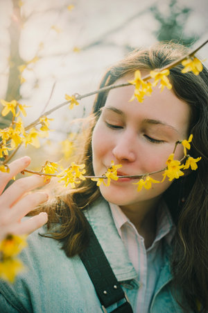 A woman stands around of yellow flowers, her eyes closed as she inhales their sweet fragrance. The breeze carries the scent through the air. This image evokes themes of nature and rejuvenationの写真素材