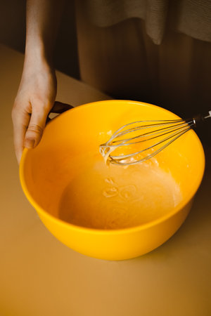 A woman whisking dough in a mixing bowl at home in her kitchen, preparing a homemade bakery delight for breakfast. Domesticity, comfort and savoring the simple pleasures of life.の写真素材
