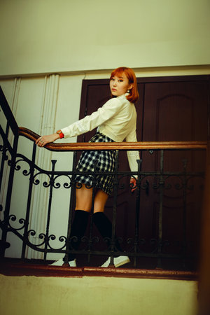 On the school staircase, a beautiful ginger Asian schoolgirl stand in uniform, holding onto the handrail. Strength of a young student navigating the challenges of academia and multiculturalism.の写真素材
