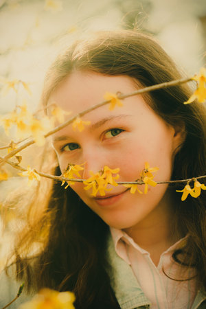 A portrait of a young and beautiful woman adorned with yellow spring flowers, taken on a sunny and warm day. It embodies themes of youth, beauty, nature, and the awakening of spring.の写真素材