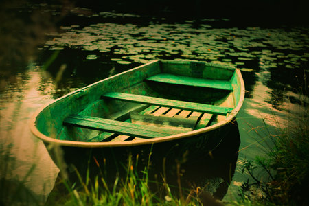 A green old fishing boat stands among the shore thickets of the pond on a summer day. Rest by the river.の写真素材