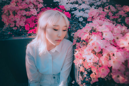 Portrait of a beautiful Asian woman with blonde hair in a blooming garden on a warm spring day. Delicate pink flowers surround her.の写真素材