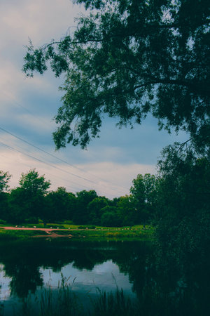 The sky above the calm lake has darkened and become overcast. A storm is approaching, and it will soon rain and thunder. In the summer, the park is a popular destination.の写真素材