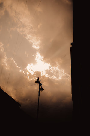 The rays of the sun shining through the clouds illuminated the city. Against the sky, his silhouette and that of a retro-style lantern were visible. Sunsetの写真素材