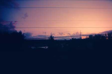 From the train window, the evening landscape is a beautiful sight. Outside, fields stretch as far as the eye can see, with power lines crisscrossing the sky as it darkens.の写真素材