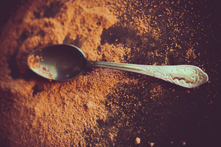 A silver tea spoon lies on the table next to a small pile of cocoa powder, creating a delicious...