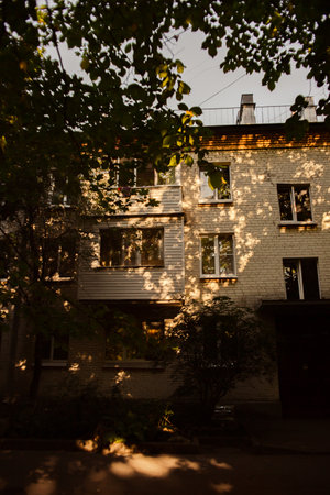 On a summer evening, the warm and cozy light of the sun shines through the leaves of the trees, casting a gentle glow on the apartment building.の写真素材