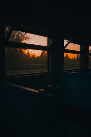 The view from the window of the train as it passes through the forest, with a beautiful orange sunset in the distance. Traveling on the train in the evening.の写真素材