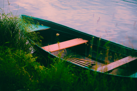 An empty wooden boat floats on the blue waters of the river near the grassy bank on a clear summer day, perfect for fishing and recreation.の写真素材