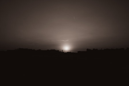 A black-and-white photograph captures the picturesque scene of the setting sun and the dark silhouettes of the cityscape. It is evening and sunset.の写真素材