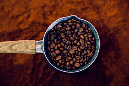 Top view of a coffee pot with a wooden handle. Inside, roasted coffee beans are placed. The coffee pot sits on top of ground coffee.の写真素材