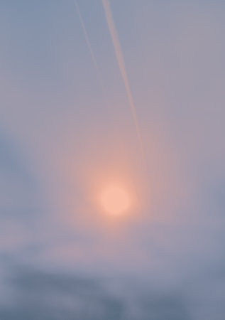 In the morning, the gentle light of the rising sun shines through the soft clouds in the sky, creating a peaceful atmosphere. Traces of flying planes can be seen.の写真素材