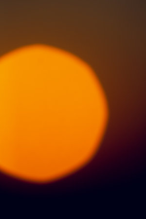 A bright, blurred solar disk against a dark orange sky at sunrise, creating a beautiful backdrop.の写真素材