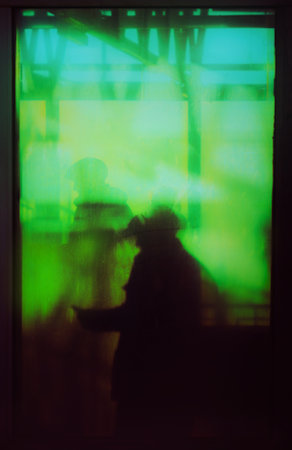 Photo of a silhouette of a man standing behind the glass window of a train station on a sunny day,...