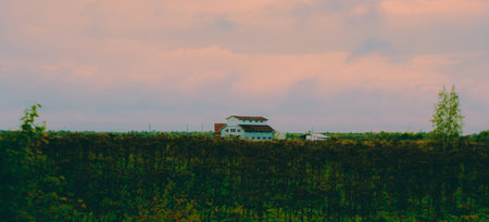 A landscape with an old wooden house, standing green in the field, with a high backdrop of a cloudy sky. A rural area.の写真素材