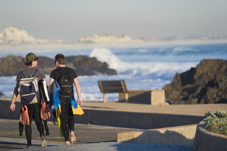 Two boys with body-boards wearing wetsuits and carrying fins, walking next to the beach.の写真素材