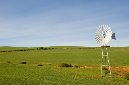 A traditional windmill turning in the wind and pumping water out of the ground into a catchment dam.