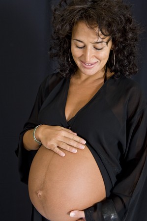 A beautiful pregnant girl showing her tummy 10 days before delivery. Black background.の写真素材