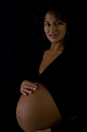 A beautiful pregnant girl showing her tummy 10 days before delivery. Low key on black background.の写真素材
