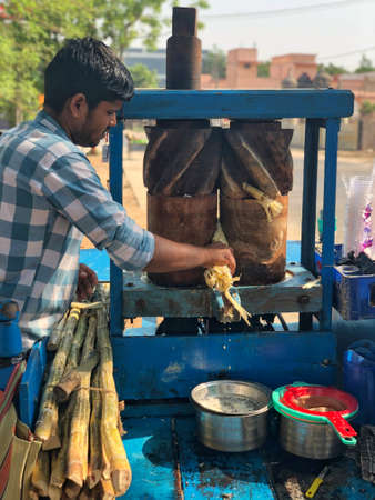 Man squeezing out sugarcane juice in a traditional machine on the roadのeditorial素材