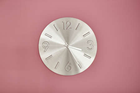 metal clock on pink painted wall. Minimal time concept.の写真素材