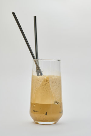 Iced coffee in a tall glass with straws on white background